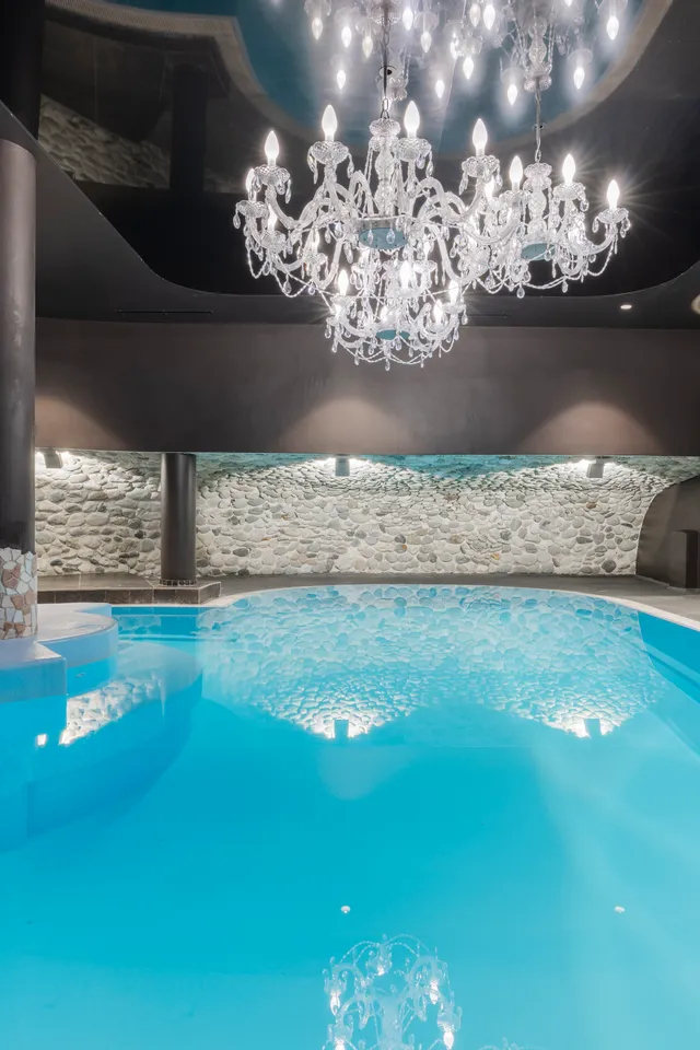Luxury indoor swimming pool with chandelier lighting and stone wall accents