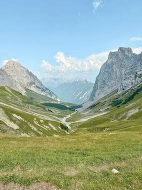 Scenic alpine valley with green meadows and rugged mountain peaks under a clear blue sky