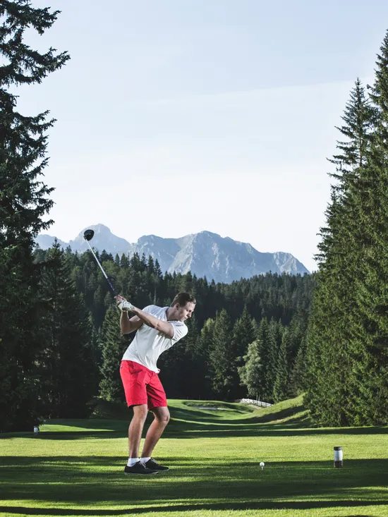 Golfer in red shorts swinging a golf club on a scenic mountain course