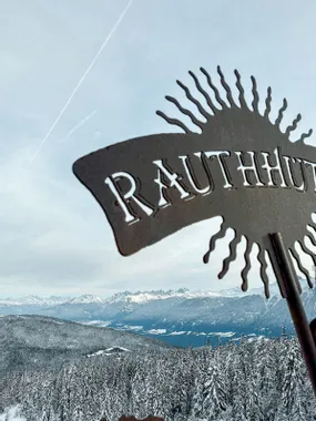 Metallschild Rauthhütte mit verschneiten Alpen und Wald im Hintergrund