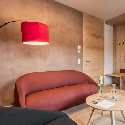 Moderne Hotelsuite mit Holzeinrichtung, roten Möbeln, Flachbildfernseher und verbundenem Schlafzimmer