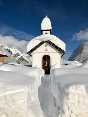 Schneebedeckte Kapelle in den Alpen mit tiefem Pfad durch frischen weißen Schnee