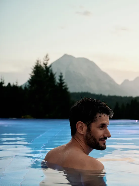 Couple relaxing in infinity pool with mountain view at sunset