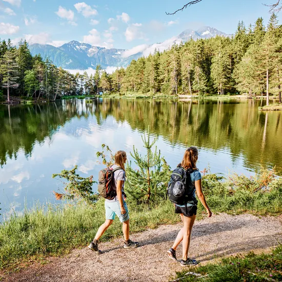 Hikers walking along a forest lake trail with mountain views in the background