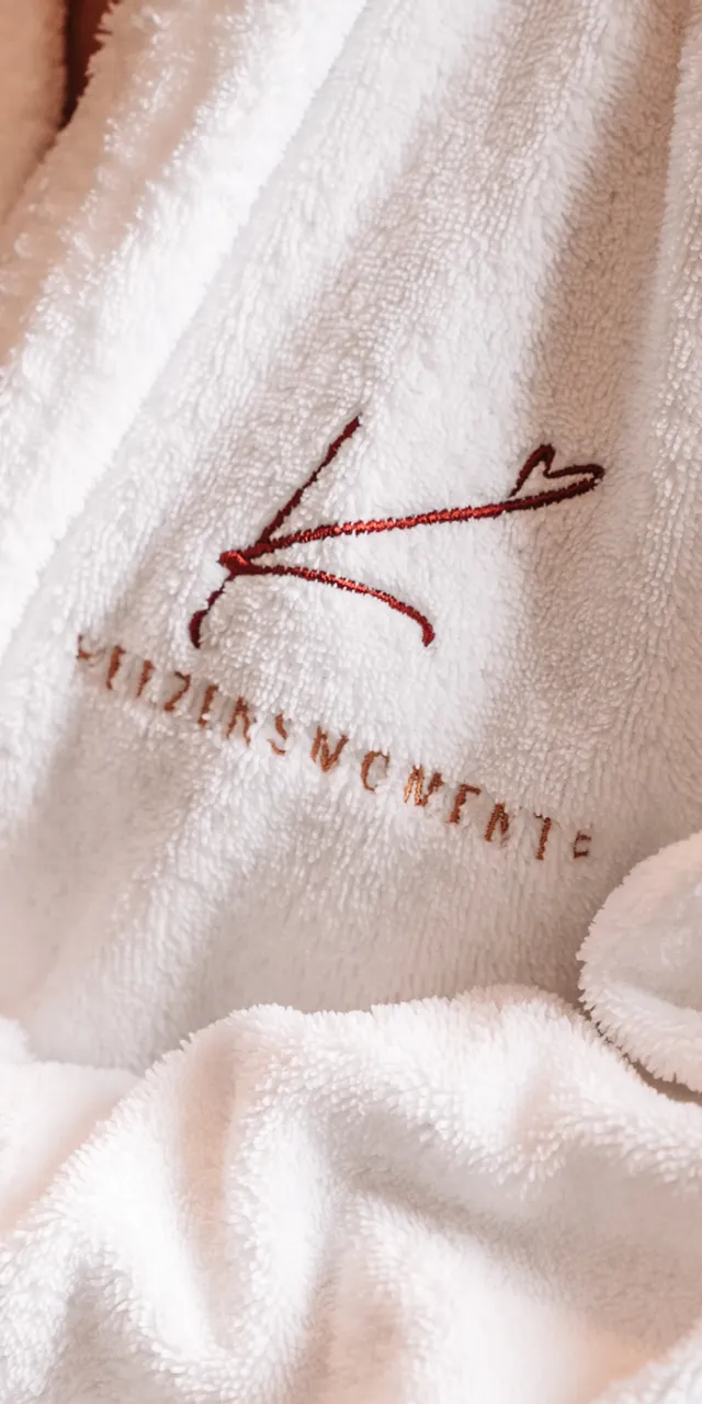 Person in white spa robe holding red apple with embroidered logo visible