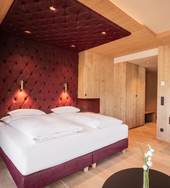 Modern hotel room with twin bed, wood paneling, mounted TV and burgundy accents