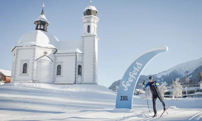 Cross-country skier at Seefeld finish line with snow-covered church and mountains
