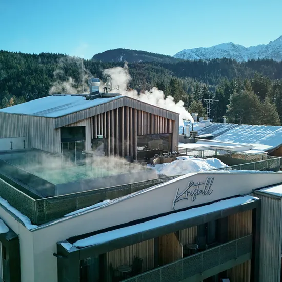 Modernes Alpenhotel mit Infinity-Pool auf dem Dach und verschneiter Bergwaldkulisse