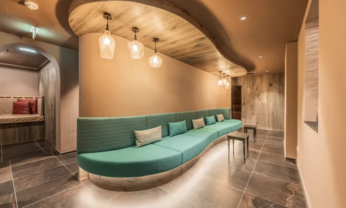 Modern spa lounge with curved teal seating, warm lighting and wooden ceiling accents