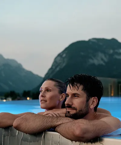 Couple relaxing in rooftop infinity pool with mountain view at dusk