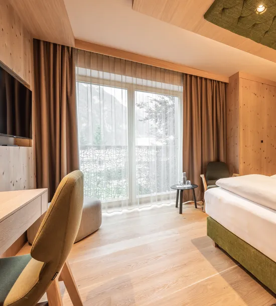 Modern hotel room with wooden interior, double bed, desk, TV and mountain view through large window
