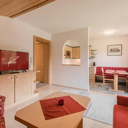 Cozy holiday apartment living room with red seating, TV, and dining nook near kitchenette