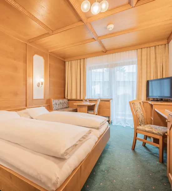 Cozy hotel room with double bed, wooden furniture, desk, TV and balcony access