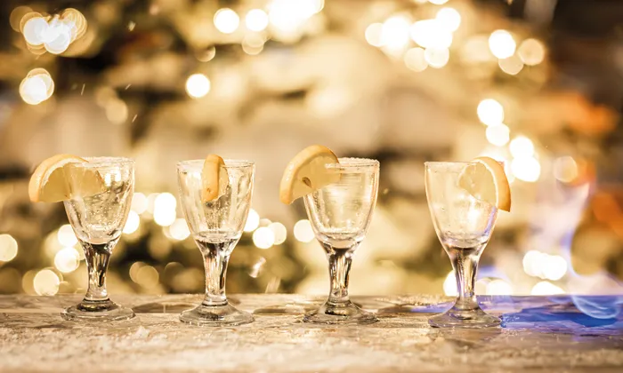Four tequila shots with lemon slices on a frosty bar with festive golden bokeh lights