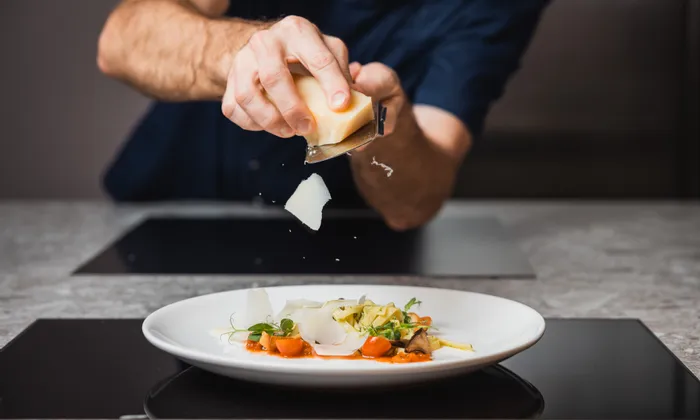 Chef grating parmesan cheese over gourmet pasta with vegetables on white plate
