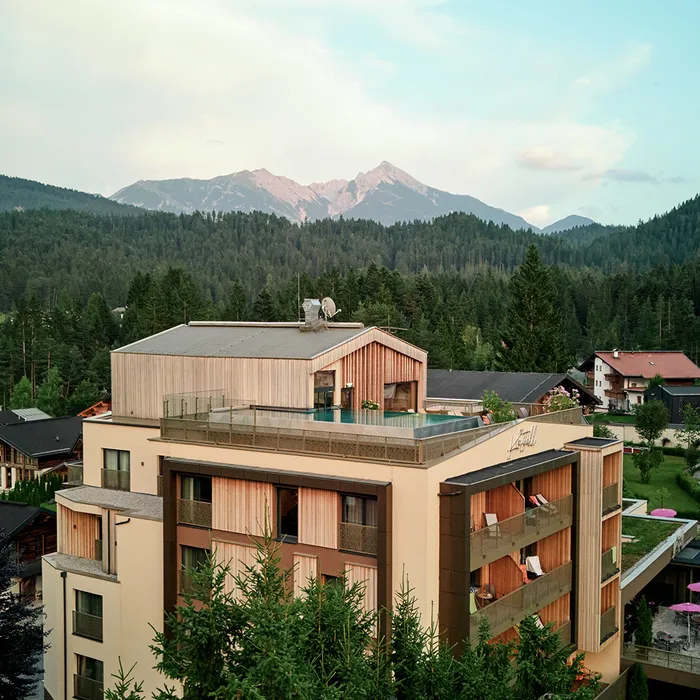 Modern alpine hotel in forested mountain village with scenic mountain range in background