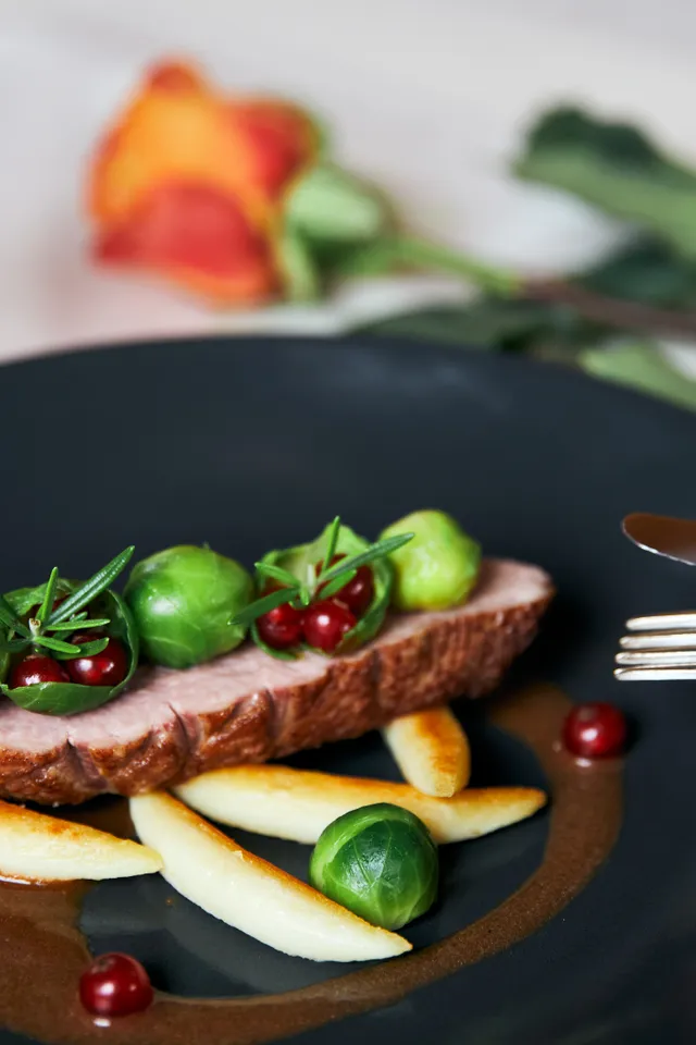 Gourmet-Entenbrust mit Rosenkohl, Preiselbeeren und Kartoffelklößen auf schwarzem Teller