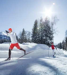 Two people cross-country skiing on a sunny winter day in a snowy mountain landscape