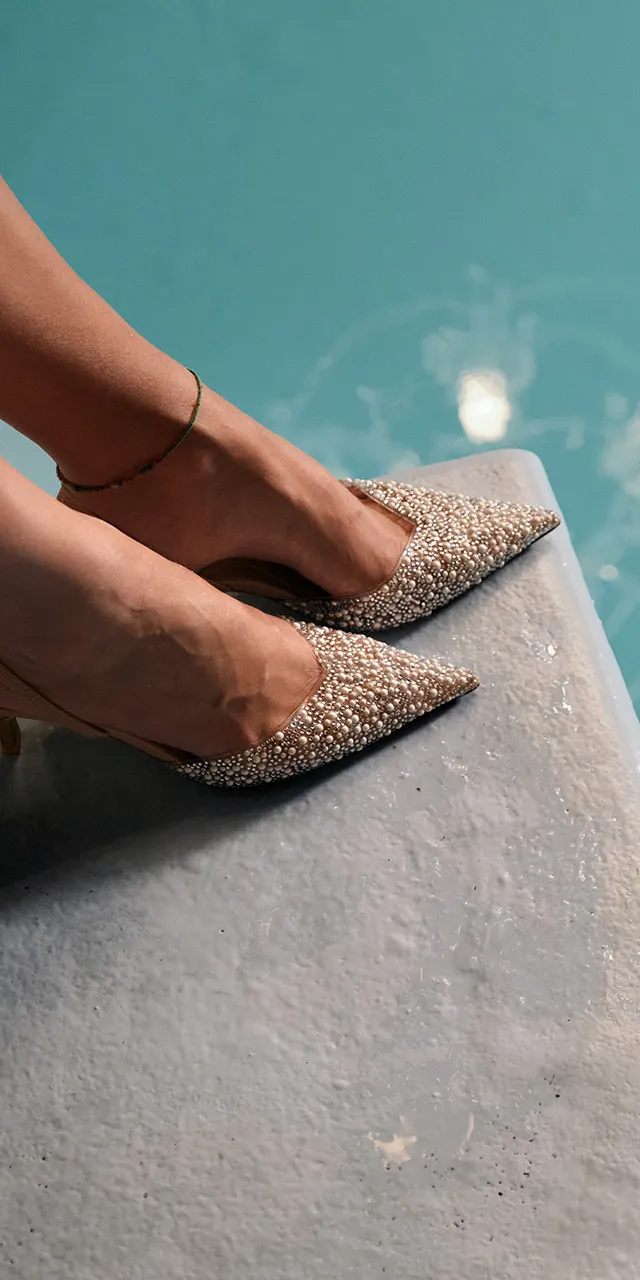 Frau mit glitzernden High Heels und Kronleuchter-Spiegelung im türkisfarbenen Wasser