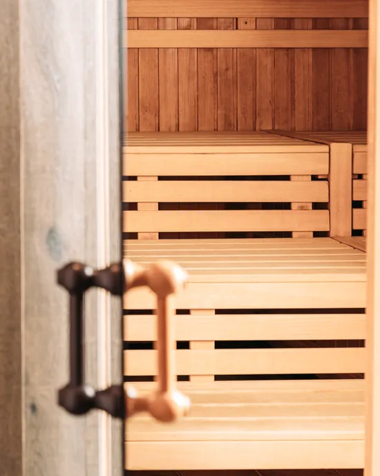 Offene Holztür einer Sauna mit sichtbaren Innenbänken aus hellem Holz