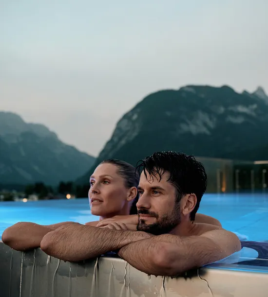 Couple relaxing in rooftop infinity pool with mountain view at dusk
