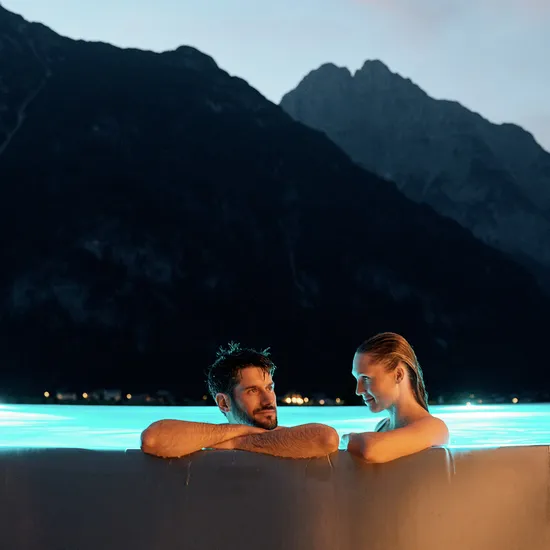 Couple relaxing in a glowing infinity pool at dusk with mountain backdrop