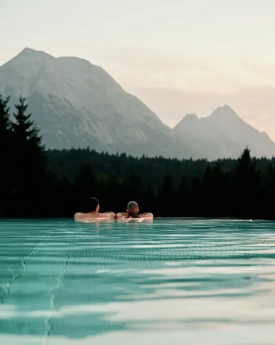 Paar entspannt im Infinity-Pool mit malerischem Bergblick bei Sonnenuntergang
