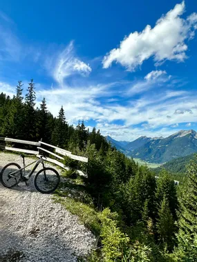 Mountain bike on gravel trail overlooking alpine valley with dense forest and blue sky