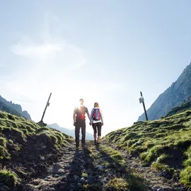 Paar wandert mit Rucksäcken auf einem Bergpfad unter klarem blauen Himmel