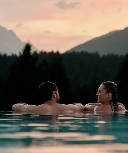 Couple relaxing in infinity pool at sunset with mountain view
