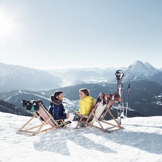 Couple relaxing on deck chairs in snowy Alps with ski gear and mountain panorama