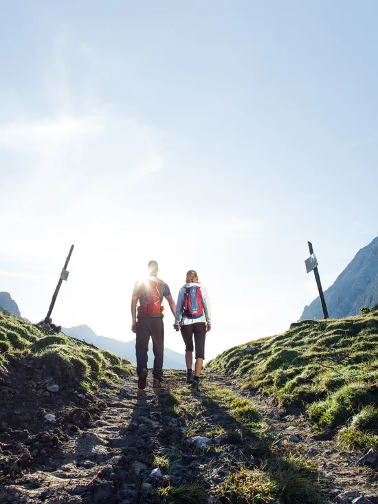 Hiking couple walking hand in hand on mountain trail at sunrise