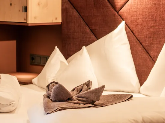 Gemütliches Hotelbett mit weißen Kissen und gefalteter Handtuch-Schwänfigur bei warmem Licht
