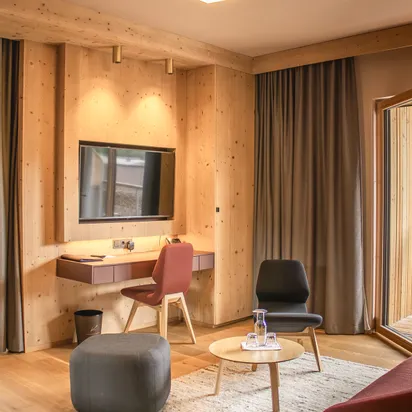 Modern hotel room with wooden walls, flat screen TV, desk, chairs, and coffee table